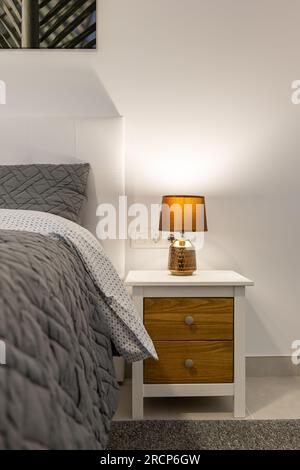 Fragment d'un lit et d'une table de chevet avec des draps gris élégants et une lampe dans une chambre compacte lumineuse. Le concept de confort et de confort Banque D'Images