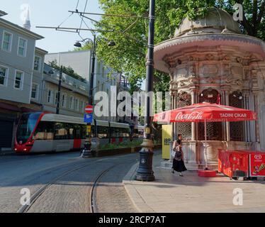 Une dame musulmane marche à côté d'un kiosque Art Nouveau avec un tramway de métro en face à Istanbul, en Turquie un matin d'été Banque D'Images