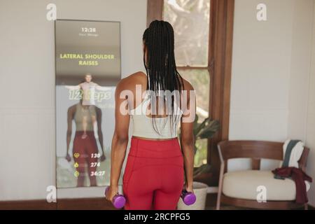 Avec l'aide d'un instructeur virtuel sur un miroir de fitness intelligent, une femme s'engage dans des exercices de musculation, en utilisant la technologie de fitness avancée à ge Banque D'Images