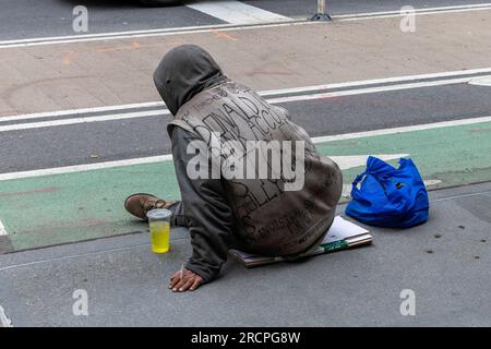 New York City, NY, USA-May 2022 ; gros plan d'une personne sans abri vue à l'arrière assise sur le trottoir d'une rue avec des vêtements sales et des écritures sur le sien Banque D'Images