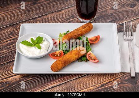 Bâtonnets de mozzarella avec des légumes verts et de la sauce sur une assiette en porcelaine blanche Banque D'Images