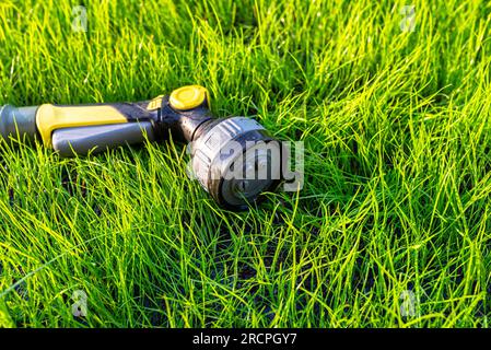 Un pistolet d'arrosage allongé sur de jeunes herbes avec un tuyau attaché. Banque D'Images