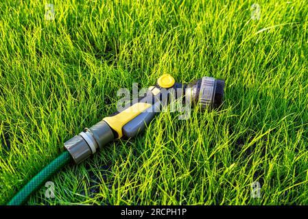 Un pistolet d'arrosage allongé sur de jeunes herbes avec un tuyau attaché. Banque D'Images