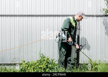 un homme tond de l'herbe à gazon avec une tondeuse à gazon. tondeuse à essence, gros plan de coupe-herbe. Homme travaillant dans le jardin Banque D'Images