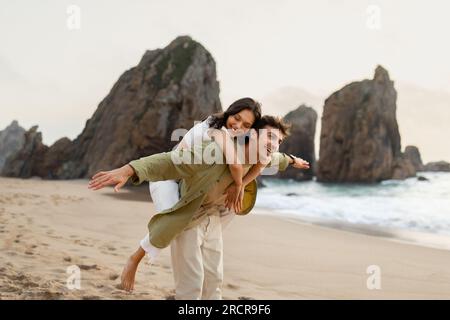 Aventure sur la plage. Jeune homme piggybacking sa petite amie et profiter du temps au bord de l'océan, espace libre Banque D'Images