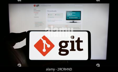 Personne tenant le téléphone mobile avec le logo du système de contrôle de version distribué Git sur l'écran en face de la page Web. Concentrez-vous sur l'affichage du téléphone. Banque D'Images