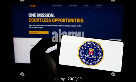 Personne tenant un smartphone avec le sceau du Bureau fédéral d'enquête (FBI) des États-Unis sur l'écran devant le site Web. Concentrez-vous sur l'affichage du téléphone. Banque D'Images