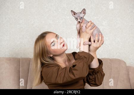 Une femme tient un petit chaton Sphynx canadien dans ses mains. Amour pour les animaux de compagnie, jour du chat. Banque D'Images