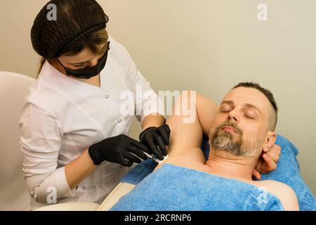 Esthéticienne fait des injections intramusculaires de toxine botulique dans l'aisselle contre l'hyperhidrose. Cosmétologie masculine. Banque D'Images