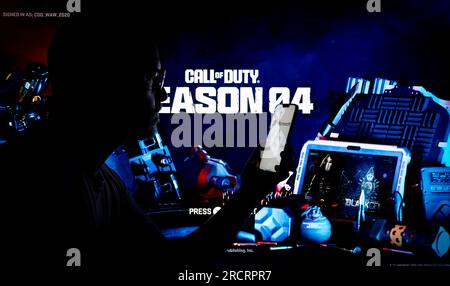 Le jeu Acitivision Call of Duty est vu en cours d'exécution sur une console PlayStation avec une personne tenant un appareil mobile au premier plan sur cette photo illu Banque D'Images