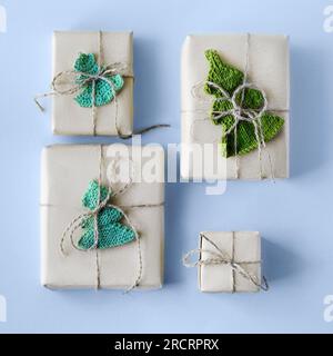 Boîtes cadeaux en papier artisanal gris décorées avec un sapin de Noël vert tricoté sur fond bleu pour les vacances, pose plate Banque D'Images
