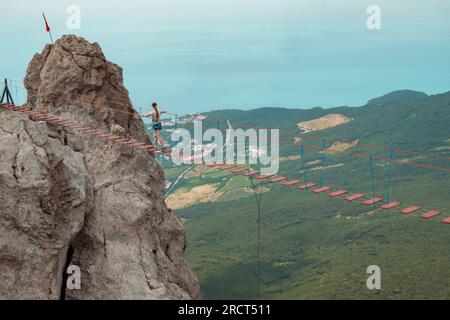 La jeune fille marche sur le pont suspendu entre les sommets des montagnes. Banque D'Images