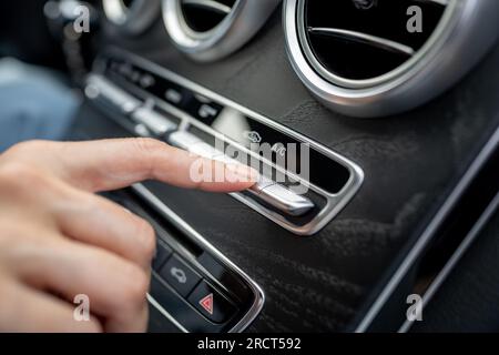 Main de femme appuyant sur le bouton allumant le climatiseur dans la voiture par temps chaud. Banque D'Images