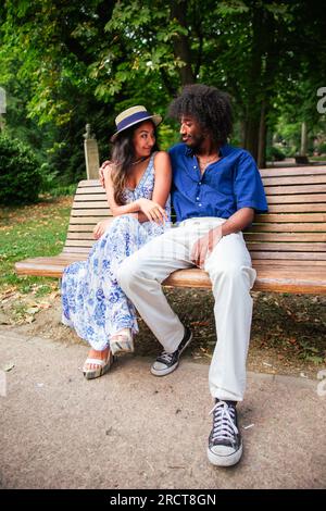 Un couple multi ethnique d'amoureux assis sur un banc conversant, photo verticale Banque D'Images