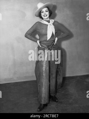 États-Unis : c. 1940 une femme attirante portant un chapeau de cow-boy, un mouchoir, des bottes et des chaps se tient souriante avec ses mains sur ses hanches. Banque D'Images