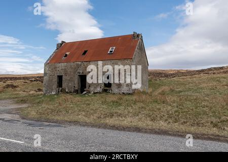 Vieille maison abandonnée dans un glen écossais contre une route avec un toit en tôle ondulée rouge Banque D'Images