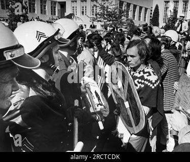 Oakland, Californie : 23 avril 1968 Un manifestant tenant un bouclier de signe de paix fait face à une ligne de police en tenue anti-émeute. Banque D'Images