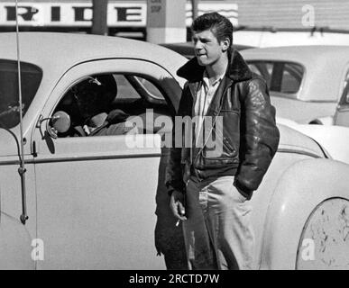 San Francisco, Californie : c.1955 Un jeune homme avec ses cheveux tranchés en arrière et son col de veste en cuir tourné vers le haut debout à côté d'une barre chaude. Banque D'Images