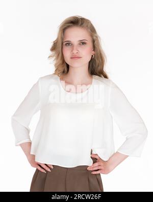 Charmante jeune femme d'affaires blonde caucasienne aux cheveux longs portant une blouse blanche et un pantalon marron. Femme européenne 21 ans regardant la caméra Banque D'Images