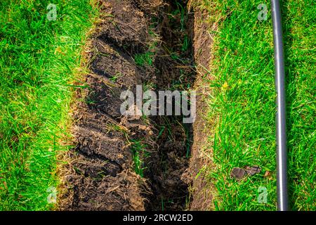 Un fossé creusé dans la pelouse pour la pose de tuyaux et l'installation d'irrigation. Sol sous pelouse verte et système de racines d'herbe Banque D'Images