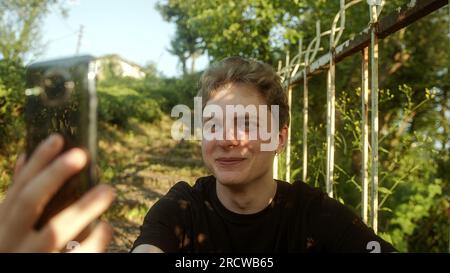 En contact avec la nature : beau Blond Jeune homme s'engageant dans un appel vidéo avec smartphone à l'extérieur Banque D'Images
