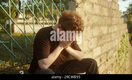 Recherche de réconfort : souligné beau Blond Jeune homme assis dans la nature, réfléchissant sur les problèmes Banque D'Images