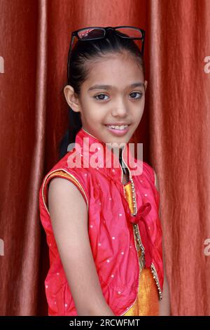 Une petite jolie fille indienne violonant avec ses lunettes dans diverses poses en robe rouge. Banque D'Images