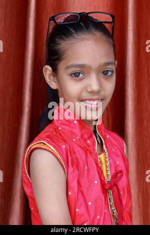 Une petite jolie fille indienne violonant avec ses lunettes dans diverses poses en robe rouge. Banque D'Images