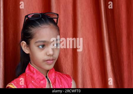 Une petite jolie fille indienne violonant avec ses lunettes dans diverses poses en robe rouge. Banque D'Images