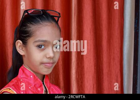 Une petite jolie fille indienne violonant avec ses lunettes dans diverses poses en robe rouge. Banque D'Images