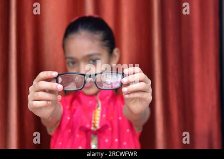 Une petite jolie fille indienne violonant avec ses lunettes dans diverses poses en robe rouge. Banque D'Images