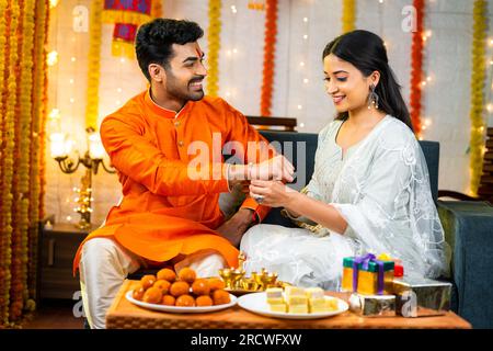 Heureuse jeune fille indienne liant rakhi à la main de frère pendant le festival raksha bandhan à la maison - concept de la culture indienne, la relation et l'occasion Banque D'Images