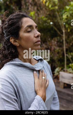 Femme biraciale faisant du yoga, méditant dans le jardin Banque D'Images