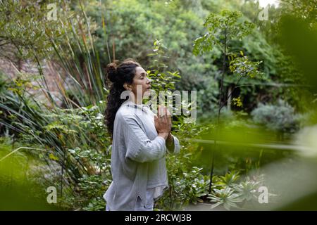 Femme biraciale faisant du yoga, méditant dans le jardin Banque D'Images