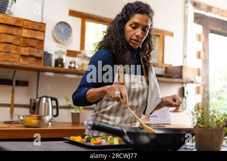 Femme biracial portant un tablier cuisinant le dîner dans la cuisine Banque D'Images