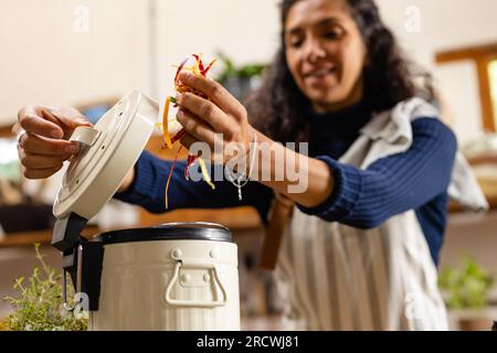 Heureuse femme biraciale portant tablier nettoyant les déchets dans la cuisine Banque D'Images