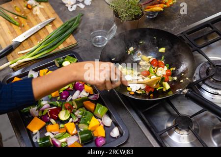 Section médiane de la femme biracial portant tablier cuisinant le dîner dans la cuisine Banque D'Images