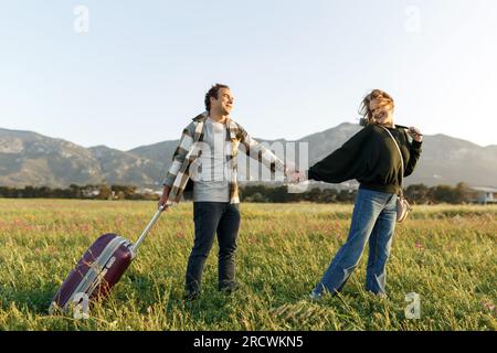 Un jeune couple épris inspiré regarde le plan de vie à l'avenir. Ils sont debout avec une valise et ukulele, tenant les mains. Recherche d'une nouvelle homela Banque D'Images