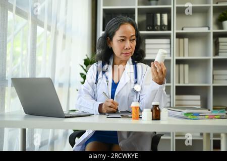 Médecin femme mature en uniforme blanc tenant une bouteille de pilules travaillant dans le cabinet médical Banque D'Images