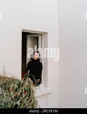 Femme élégante souriant à la caméra d'un cadre de fenêtre blanc Banque D'Images