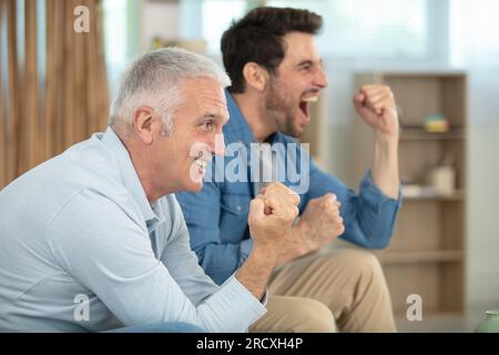 fils et père qui regardent un match de football lèvent la main en acclamant Banque D'Images