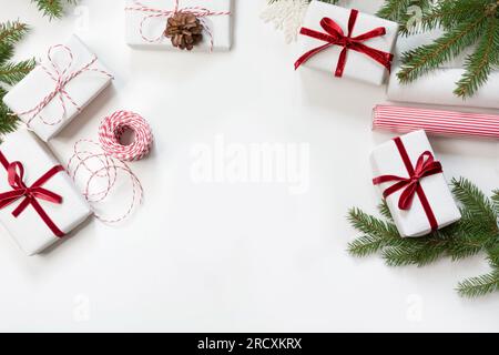 Boîtes-cadeaux de Noël enveloppées dans du papier artisanal blanc et ruban de corde rouge décoratif sur fond blanc. Pose à plat. Vue de dessus. Banque D'Images