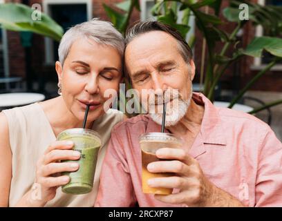 Couple mûr buvant un smoothie. Femme et mari boivent des cocktails tout en étant assis tête à tête avec les yeux fermés. Banque D'Images