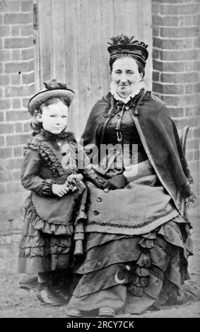 Portrait extérieur d'une dame assise avec un enfant debout à côté d'elle. Les deux portent des robes et des chapeaux foncés superposés. Photographie originale de F. Spalding de Tindall Square, Chelmsford. D'une collection de photographies victoriennes carte de visite, datées des années 1890 Carte de visite est un terme français connu en anglais sous le nom de « Visiting card ». Ils avaient généralement un tirage photographique albumen d'environ 54x89mm monté sur une carte légèrement plus grande. Dans certains cas, les ravages du temps ont fait leurs ravages. Banque D'Images