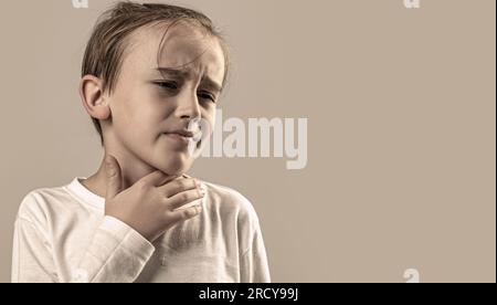 L'enfant a mal à la gorge. Jeune garçon sent que sa gorge est douleur. Petit garçon malade avec mal à la gorge. Enfant malade avec mal à la gorge. Maux de gorge dans un Banque D'Images