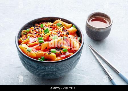 Rabokki, tteokbokki ou topokki avec ramen, cuisine de rue coréenne, gâteaux de riz épicés, baguettes et boisson Banque D'Images