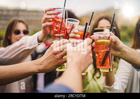 Un groupe multiracial de jeunes amis, portant des lunettes de soleil, toast avec des verres en plastique remplis de cocktails Spritz. Concentrez-vous sur les mains, les visages flous dans le Banque D'Images