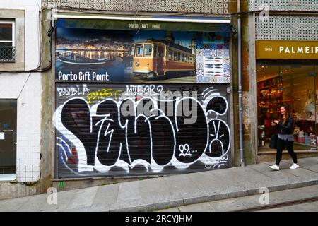 Jeune femme marchant devant des graffitis sur les volets métalliques de la boutique de souvenirs Porto Gift point, Porto / Porto, Portugal Banque D'Images