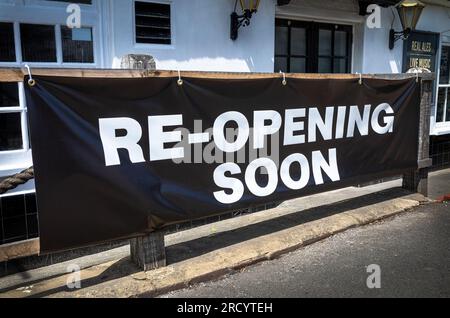 Un grand panneau imprimé sur une feuille de plastique indiquant « Re-opening Soon » apposé à l'avant d'un pub à Billingshurst, West Sussex, Royaume-Uni. Banque D'Images