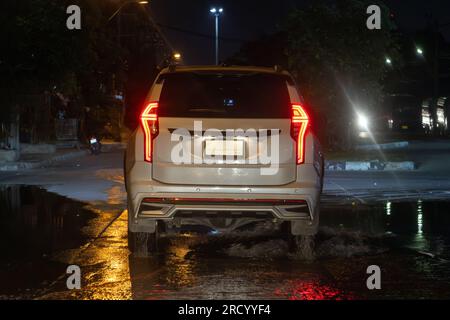 Une voiture traverse une flaque dans une rue de nuit Banque D'Images